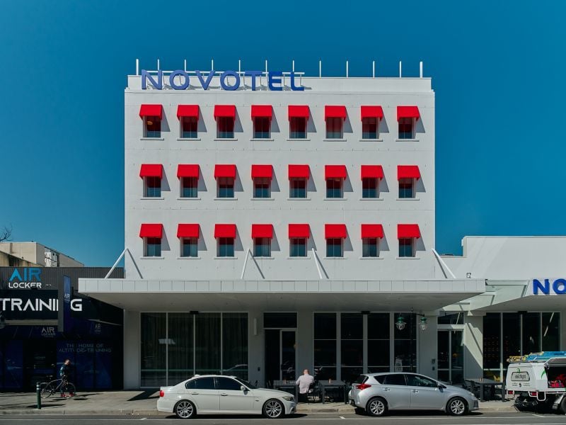 The completed Novotel St Kilda on Fitzroy Street: a white facade with red window awnings over the glazed ground floor.